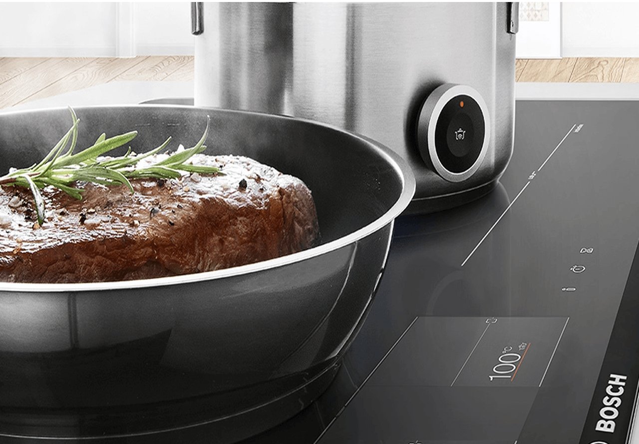 Zbliżenie na płytę indukcyjną Bosch z widocznymi polami grzewczymi. Na płycie stoją garnki z jedzeniem