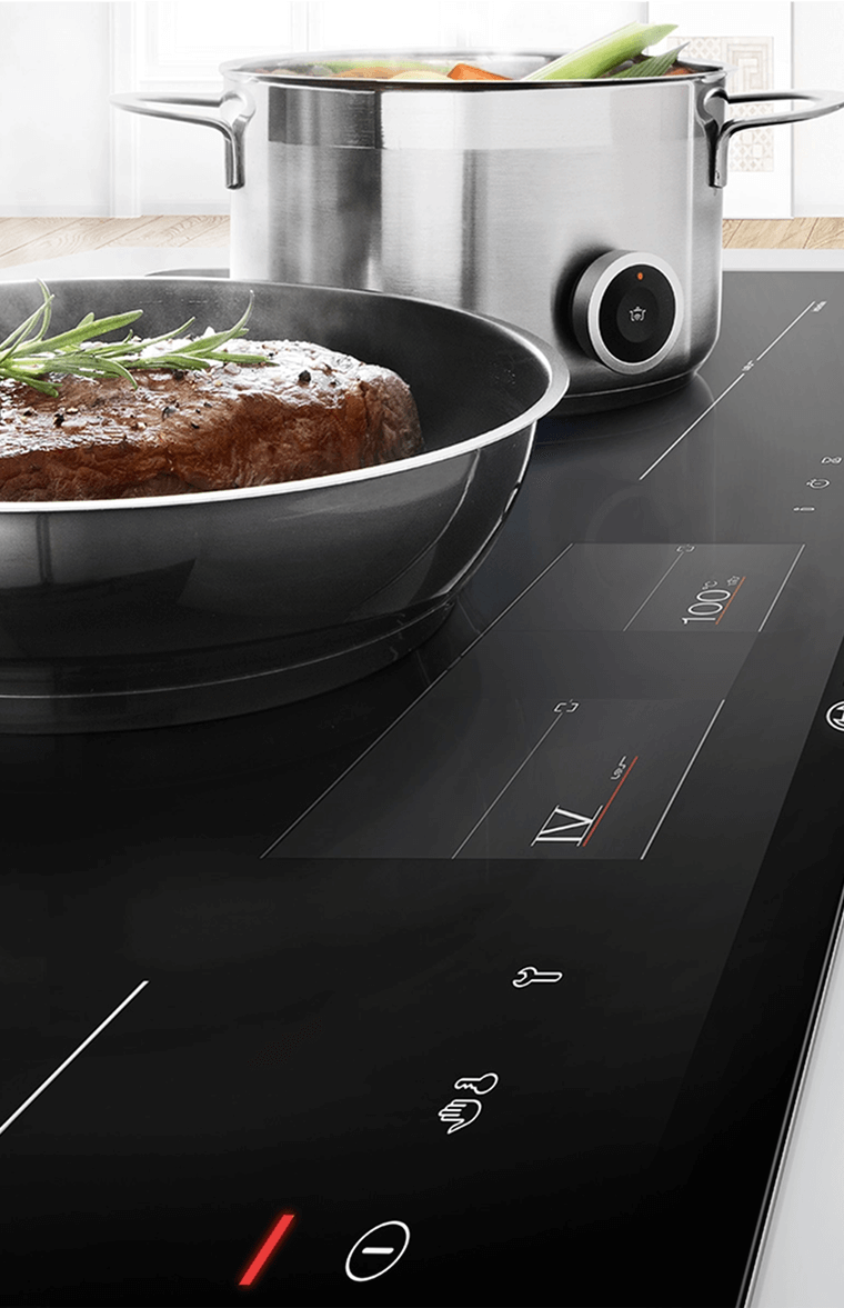 Zbliżenie na płytę indukcyjną Bosch z widocznymi polami grzewczymi. Na płycie stoją garnki z jedzeniem