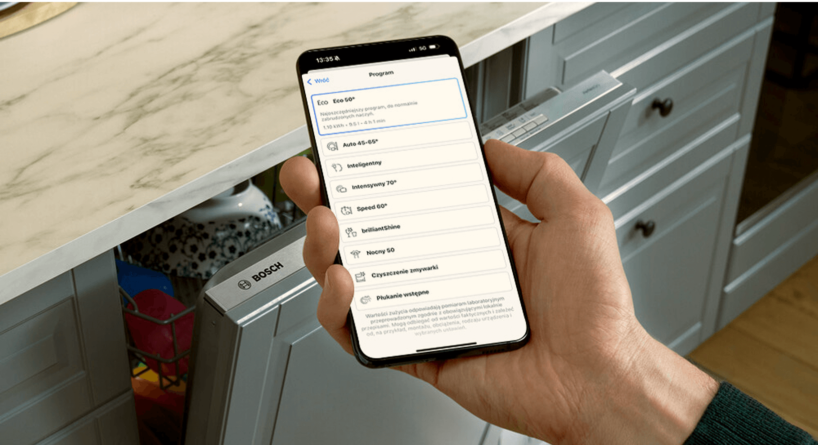 Smartfon z aplikacją Home Connect monitorująca cykl pracy zmywarki Bosch. W tle zmywarka