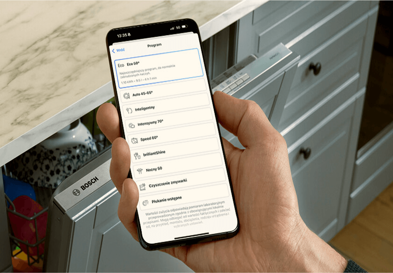 Smartfon z aplikacją Home Connect monitorująca cykl pracy zmywarki Bosch. W tle zmywarka