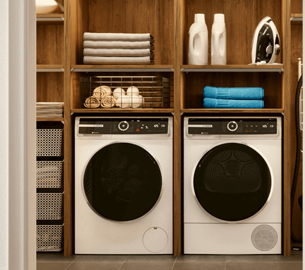 Smartfon z aplikacją Home Connect do zdalnego sterowania urządzeniami AGD Bosch. W tle pralka i suszarka Bosch.