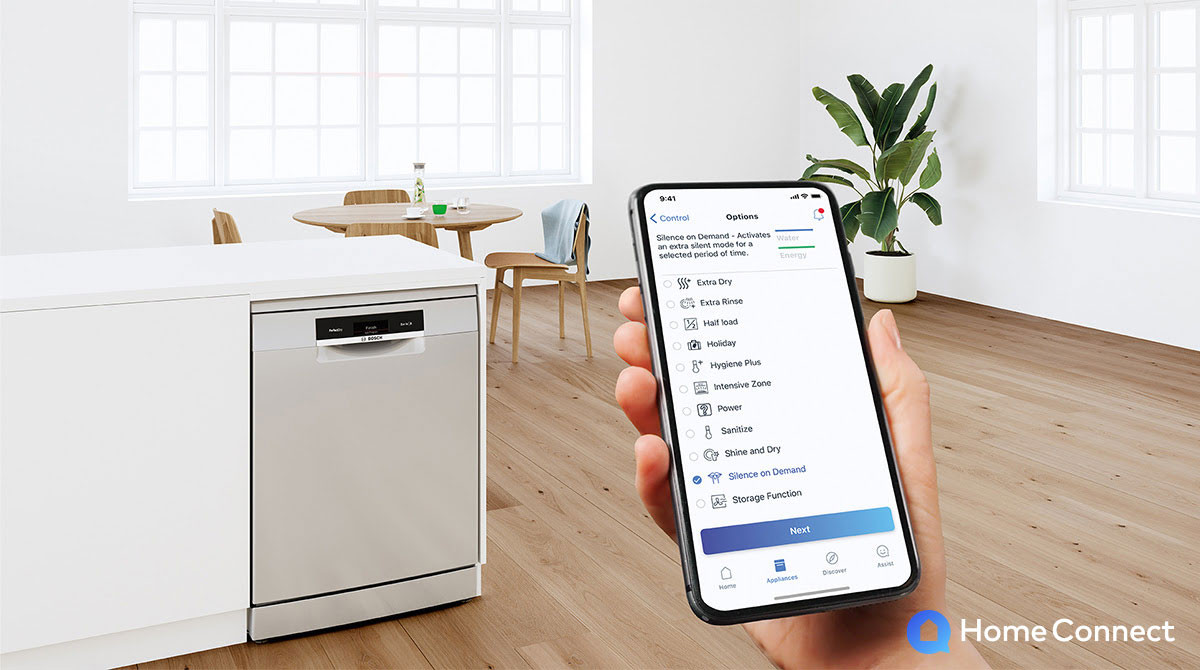 Ręka trzymająca smartfon, na nim aplikacja Home Connect z wyborem trybu pracy zmywarki. w tle Zmywarka marki Bosch